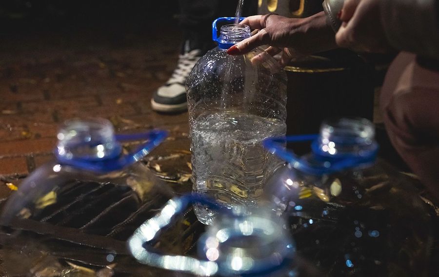 Людина набирає воду з крана в пластикові бутлі.