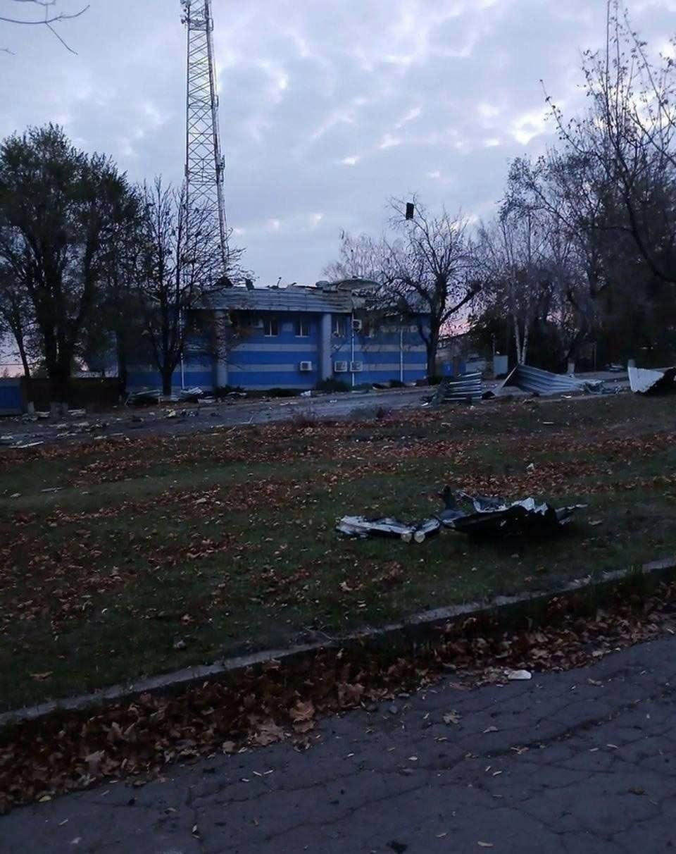 Двоповерхова синьо-сіра будівля з пошкодженим дахом, поруч розкидані уламки металевих конструкцій.