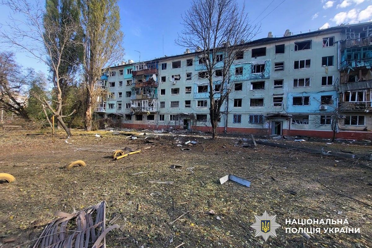 Пошкоджені багатоповерхівки з вибитими вікнами та зруйнованими балконами. На подвір’ї уламки та понівечені автомобілі.