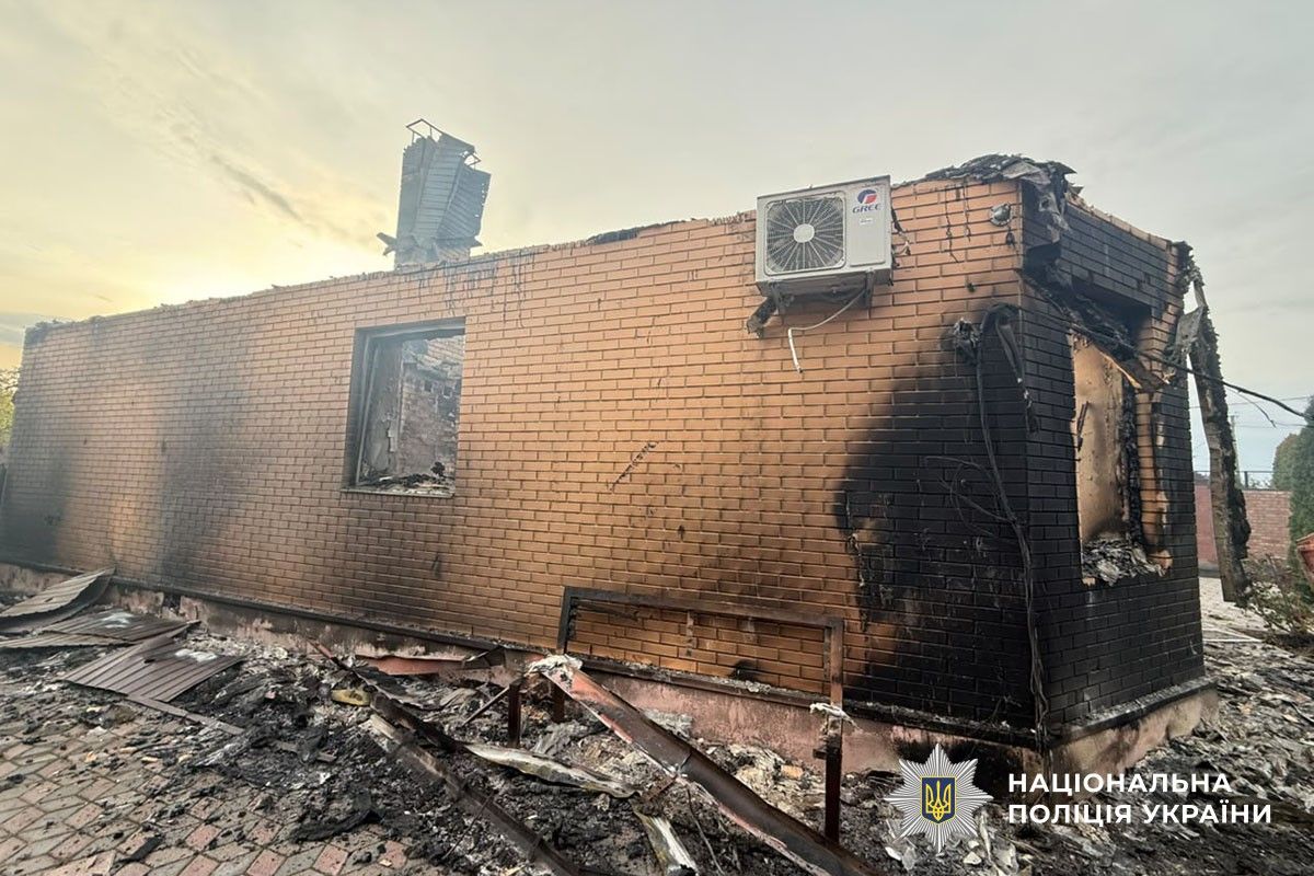 Обгорілий цегляний будинок із пошкодженим дахом та уламками зруйнованих конструкцій поруч.