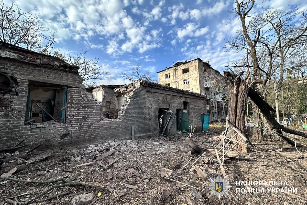 Фасад багатоповерхівки з вибитими вікнами та зруйнованими балконами. Перед будинком уламки й поламані дерева.